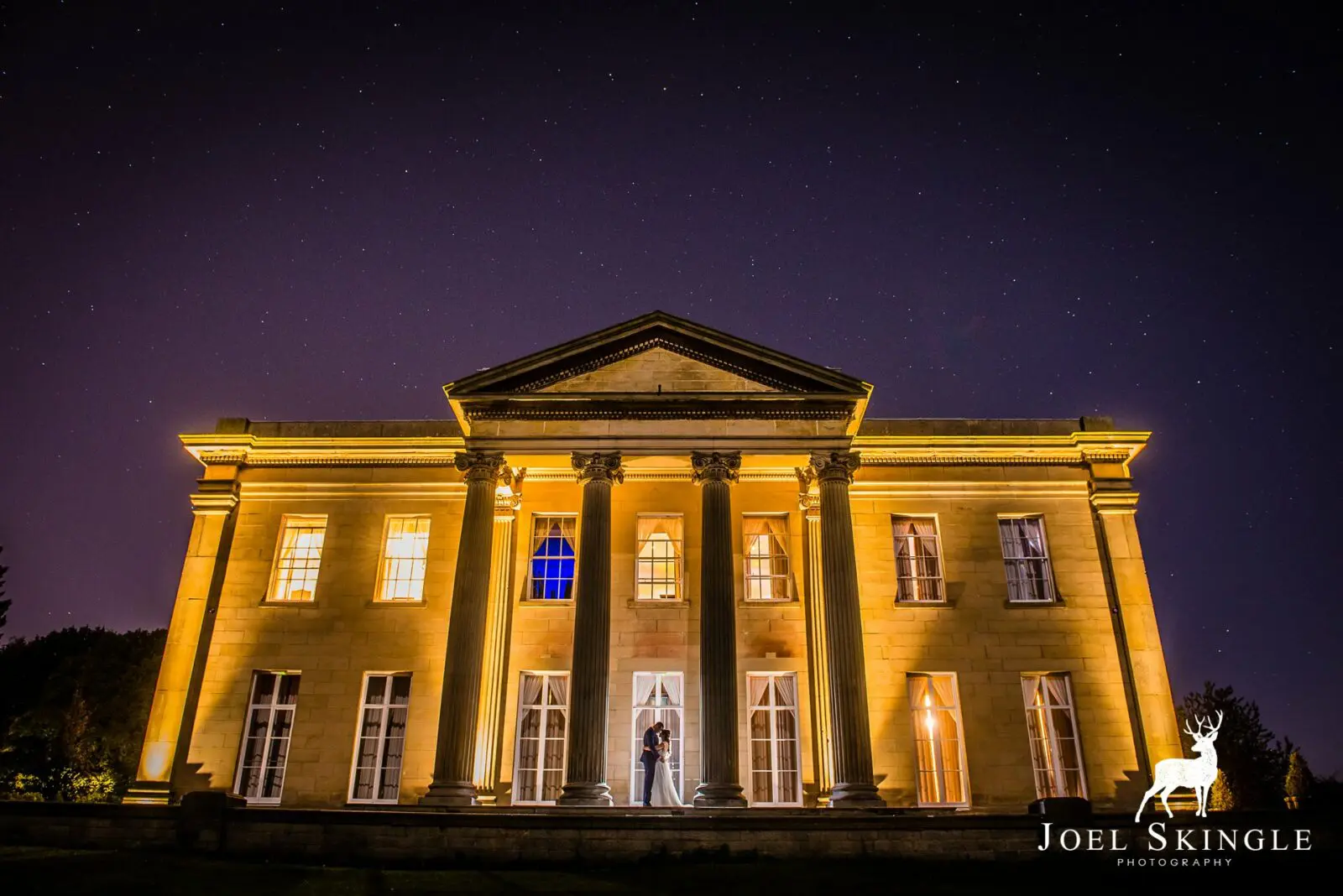Dine | Exclusive Weddings & Events in Yorkshire | A grand, illuminated neoclassical building with tall columns stands under a starry night sky, perfect for luxury Yorkshire weddings. A couple at the entrance casts shadows on the steps. Photography credit: Joel Skingle.