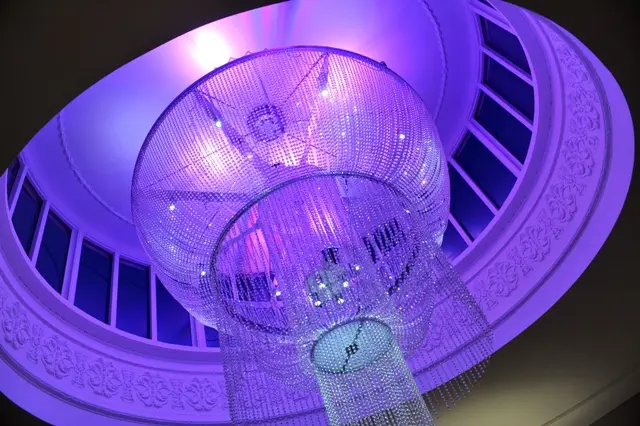 Dine | Exclusive Weddings & Events in Yorkshire | A lavish crystal chandelier hangs from a domed ceiling, illuminated by purple lighting. Perfect for Yorkshire weddings, the intricate design creates a luxurious ambiance for unforgettable events.